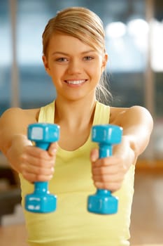 Happy girl stretching her hands with blue dumbbells during workout