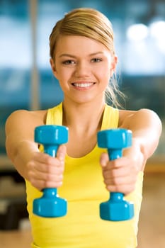 Happy girl stretching her hands with blue dumbbells during workout