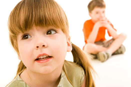 Close-up of little curious girl looking slightly aside on the background of sitting boy