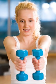 Happy girl stretching her hands with blue dumbbells during workout