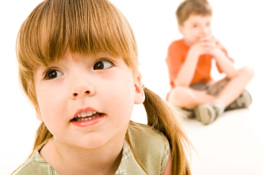 Close-up of little curious girl looking slightly aside on the background of sitting boy