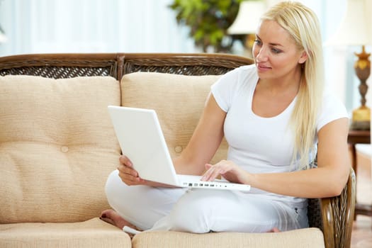 Portrait of charming blonde sitting on sofa and typing