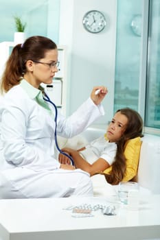 Portrait of clinician in eyeglasses looking at thermometer with sick girl lying near by