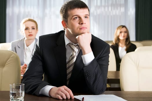 Portrait of boring man sitting at the table and two women on the background