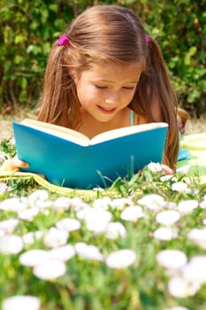 Portrait of cute schoolgirl reading interesting book in natural environment