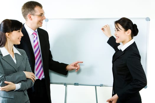 Photo of young businesswoman showing something on whiteboard with smile while her colleagues looking at it