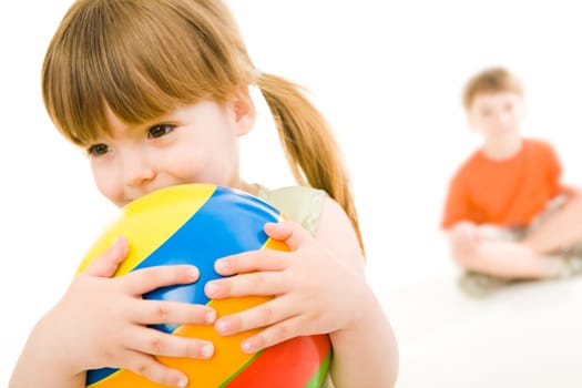 Photo of little girl holding colorful ball in hands with her brother at the background