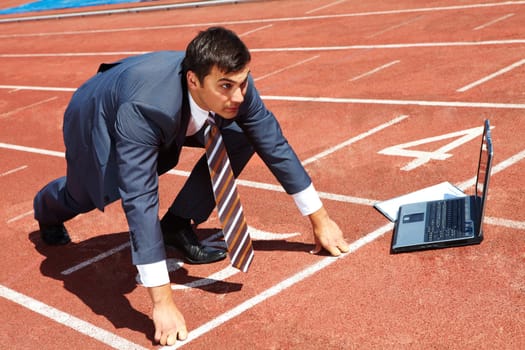 Image of businessman getting ready for race with laptop near by