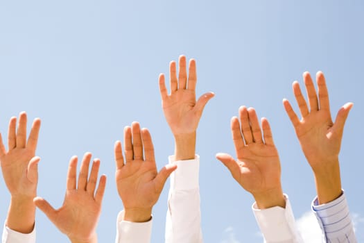 Close-up of several human hands raised against clear blue sky