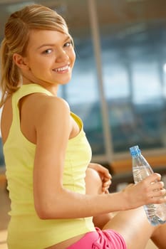 Portrait of cheerful girl holding bottle of water in hand and smiling at camera