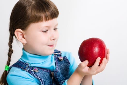 Portrait of little girl holding big red apple in hands and watching at it