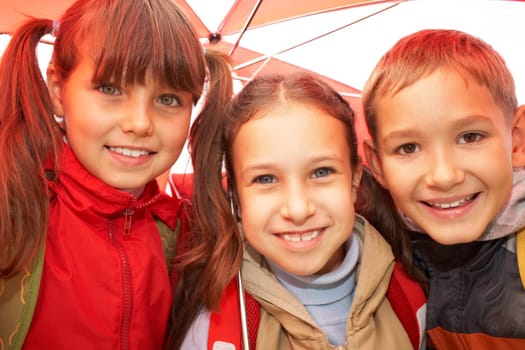Portrait of happy kids looking at camera while under umbrella outside