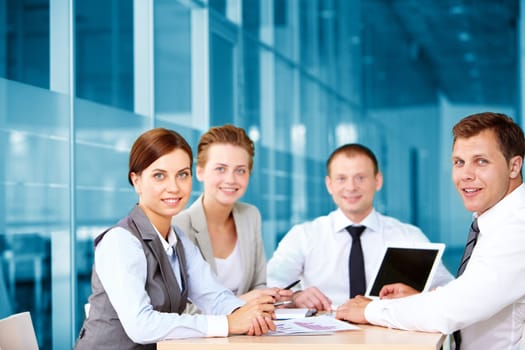 A business team of four sitting at table and looking at camera