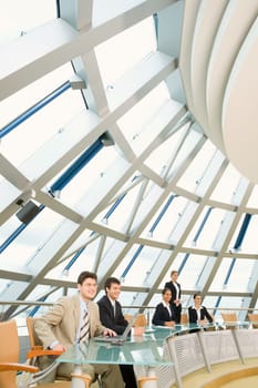 Confident professionals are sitting at the glassy table in large room and discussing  business questions