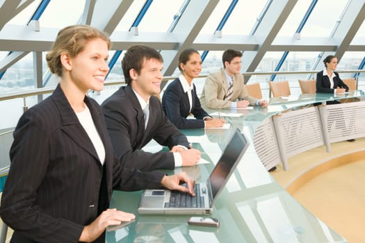 Businesspeople sitting at the round table in large light conference hall with glassy walls discussing important questions