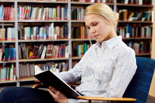 Portrait of clever student with open book reading it in college library