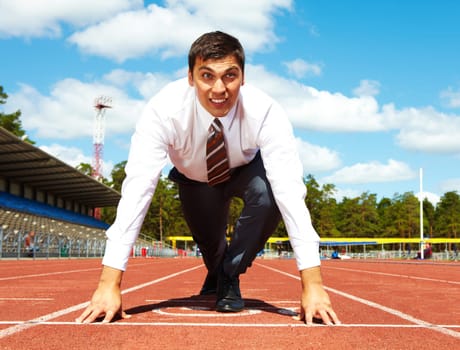 Image of handsome businessman getting ready for race at stadium