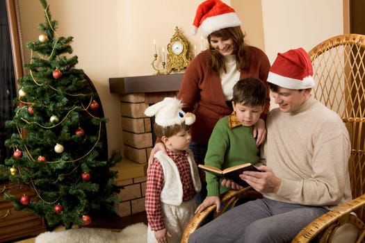 Portrait of family gathered together to read interesting fairy tale with decorated fir tree behind