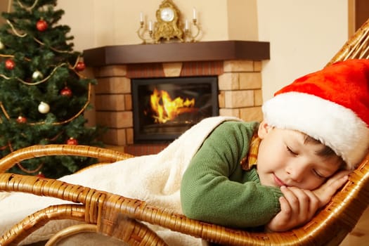 Photo of cute infant wearing santa cap sleeping in rocking chair under blanket