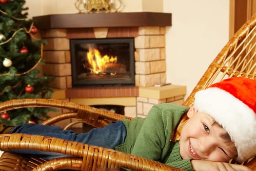 Photo of cute boy wearing santa cap pretending to sleep in rocking chair