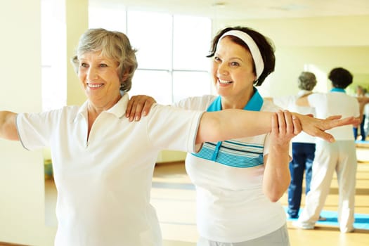 Portrait of sporty female supporting her friend while doing physical exercise in sport gym