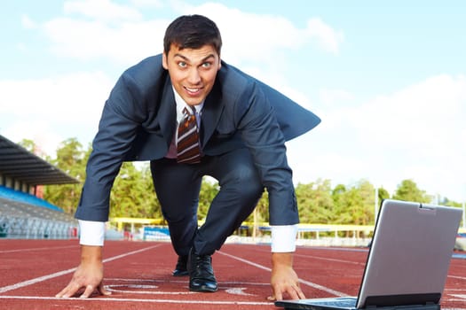 Image of businessman getting ready for race with laptop near by