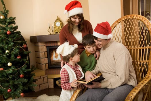Portrait of smiling man with book in hand sitting in rocking-chair and looking at his little sons standing near by
