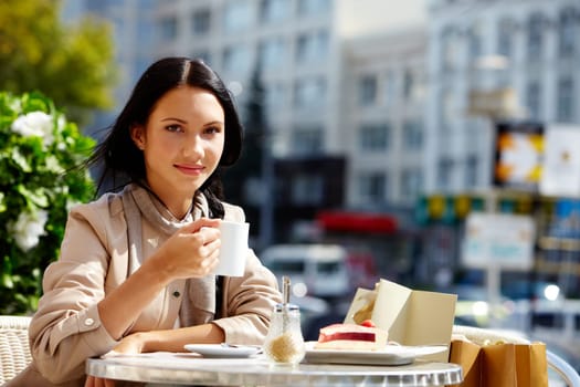 Image of young brunette in open air cafe looking at camera in urban environment