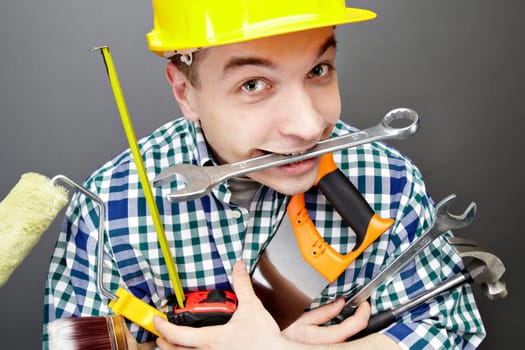 Portrait of happy craftsman with different tools in hands and wrench in mouth