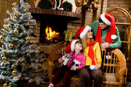 Portrait of happy family wearing santa caps while sitting by fireplace and looking at each other