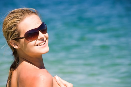 Portrait of beautiful female in sunglasses on background of blue ocean