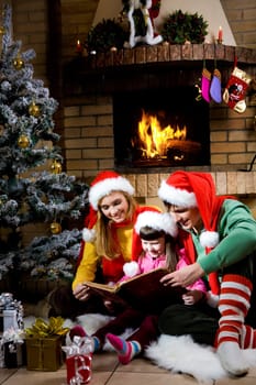 Portrait of family spending Christmas evening at reading book by fireplace