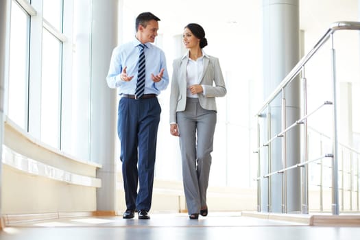 Confident business partners walking down in office building and discussing work