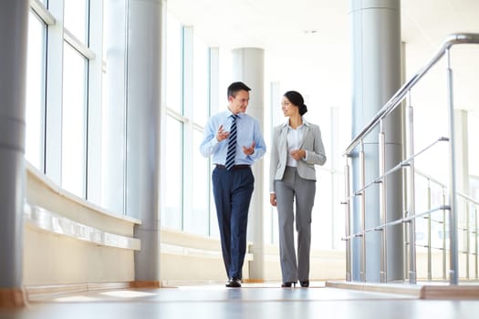 Confident business partners walking down in office building and talking