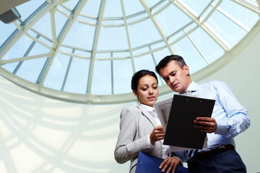 Image of confident businessman looking at document in partners hand while discussing it