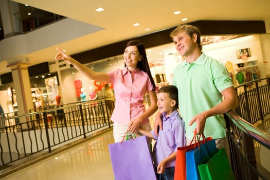 Portrait of pretty female showing something to her husband and son during shopping