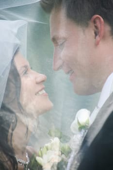 Face of newly wedded looking at each other under veil