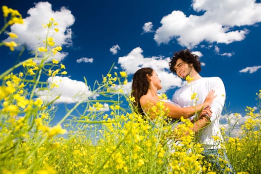 View of amorous couple in golden meadow under summer sky with clouds on it