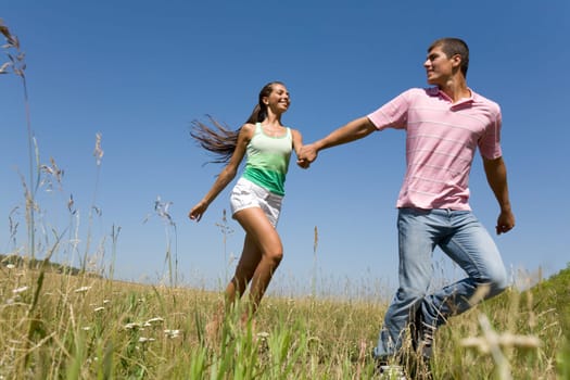 Photo of young man and woman holding each other by hands and running outdoors
