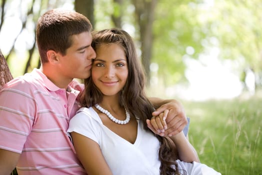 Image of tender man kissing girls face while she smiling at camera in natural environment