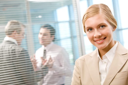 Portrait of happy businesswoman smiling at camera on background of interacting men