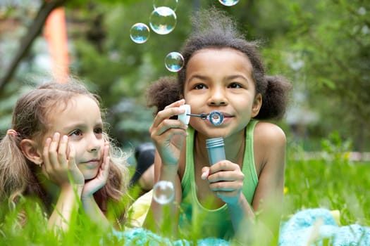 Portrait of cute girl blowing soap bubbles with her friend near by