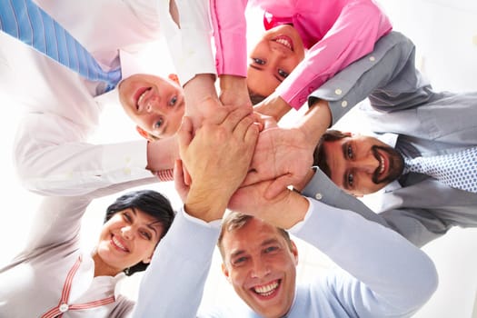 Below shot of smiling co-workers making pile of hands and looking at camera