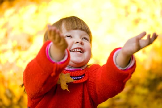 Cute girl laughing and playing with autumn leaves in park