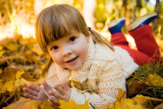 Small adorable girl lying on golden leaved ground in autumn and enjoying herself