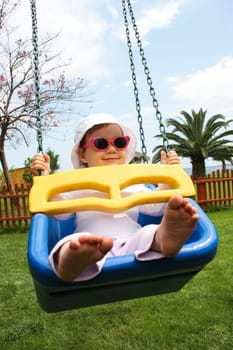 Portrait of happy baby in cap and sunglasses swinging during summer vacations on resort