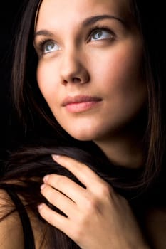 Image of young female with dark hair touching it by hand