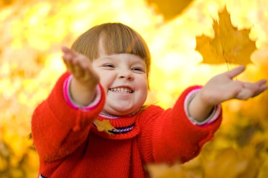 Very cheerful child having fun while tossing up yellow leaves
