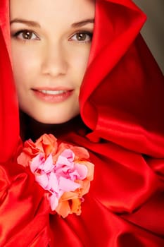 Gorgeous woman in red satin holds flower looking at camera