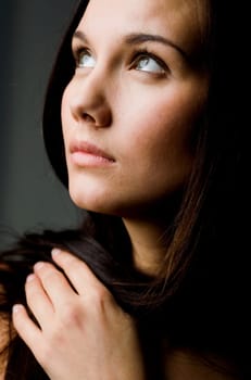 Image of young female with dark hair touching it by hand and looking upwards
